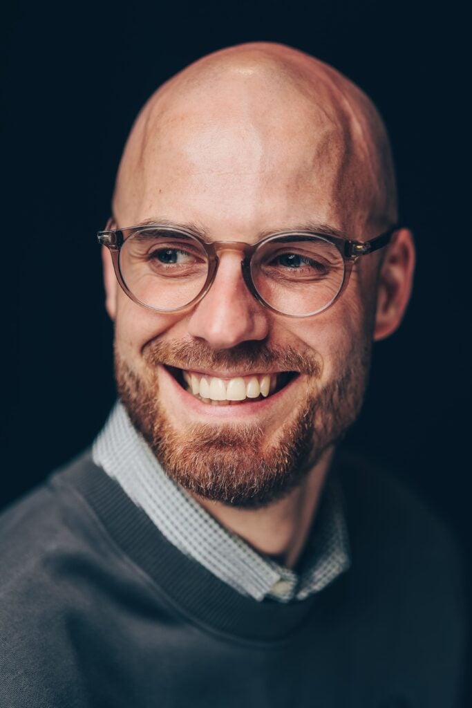 Lächelnder Mann mit Glatze und Brille, der in die Kamera schaut.