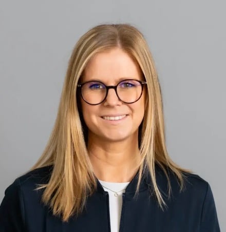 Porträt einer Frau mit langen blonden Haaren und Brille, die in die Kamera lächelt.