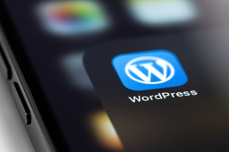 Auf einem Smartphone-Display ist das blaue WordPress-Logo mit der Bezeichnung WordPress zu sehen.