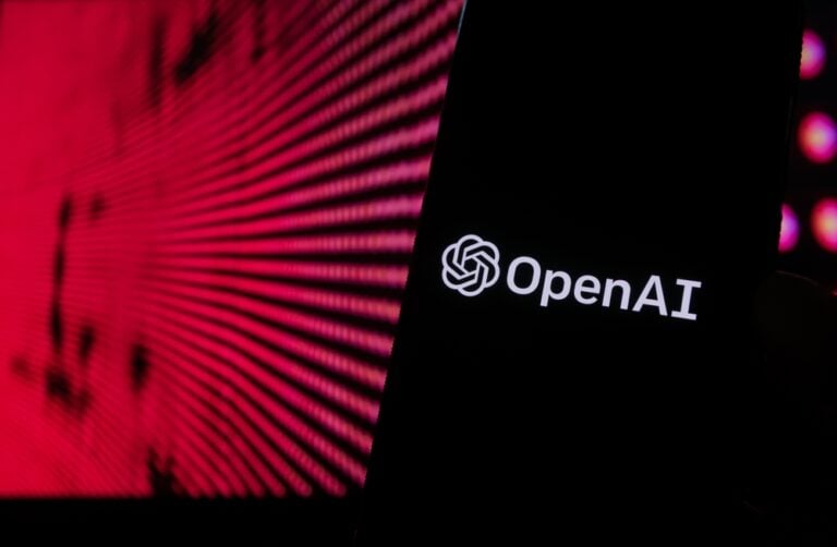 The OpenAI logo glows on a black screen in front of a red-patterned digital representation of ChatGPT.