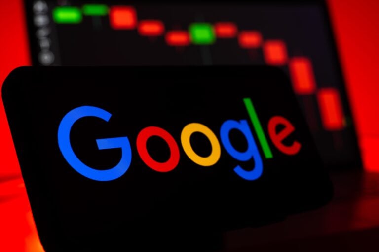 Auf einem schwarzen Display steht das farbige Google-Logo vor einem unscharfen Kursdiagramm mit überwiegend roten Balken; Thema ist AI Max.