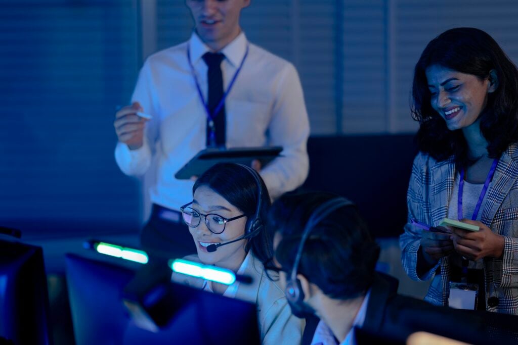 In blauem Licht arbeiten mehrere Teammitglieder mit Headsets und Tablet zusammen in einer Leitstelle und tauschen sich konzentriert über Daten aus.